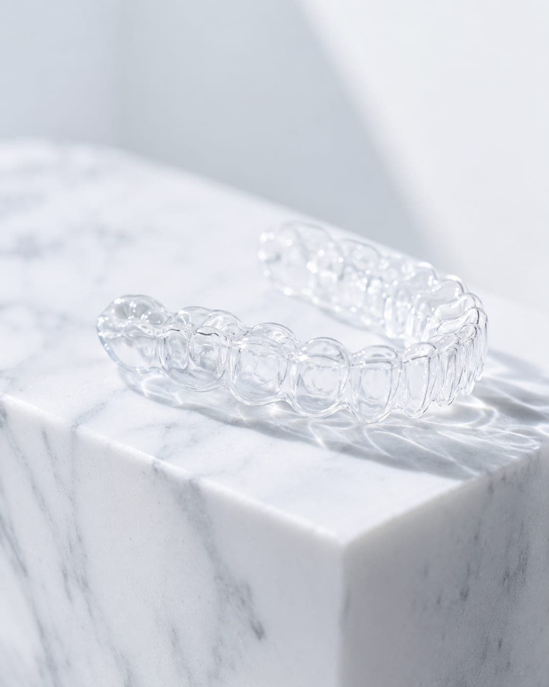 Clear aligners — a transparent tray catching the light on marble